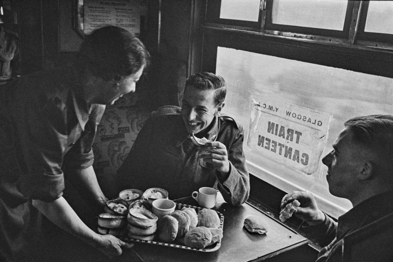 A female worker from the Young Men’s Christian Association (YMCA) serves pies and rolls to British servicemen from their on-board canteen in a train carriage during a railway journey from Glasgow