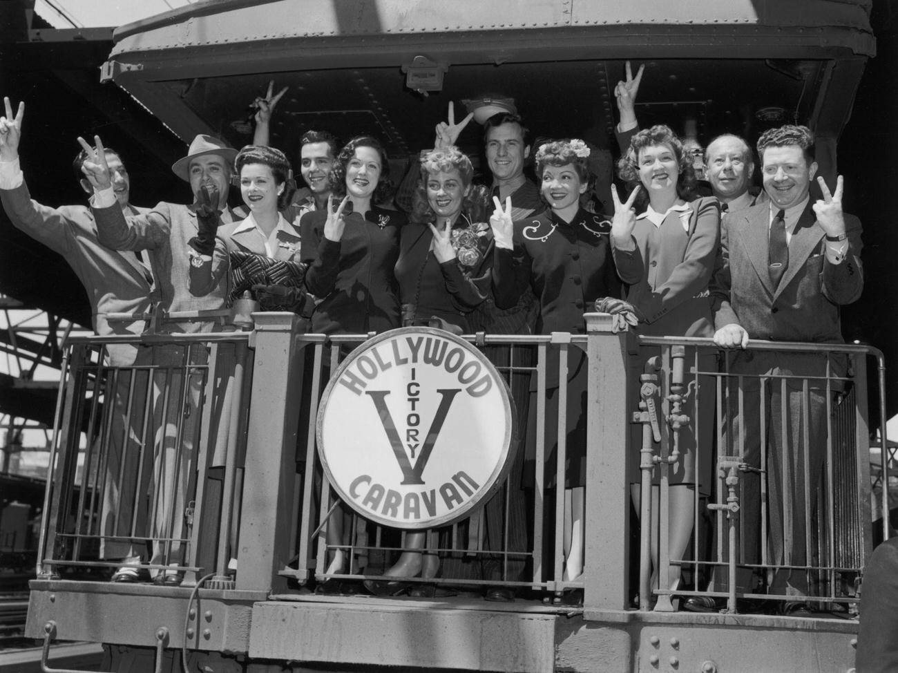 Members of the Hollywood Victory Caravan make a ‘V’ for ‘Victory’ sign while standing at the back of a railroad car.