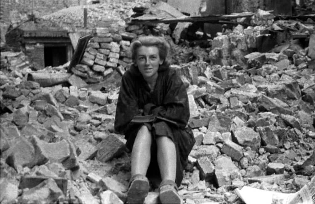 #26 Girl from Anna Company of the Gustaw battalion reading a book amid the rubble on Ślepa Street in the Old Town.