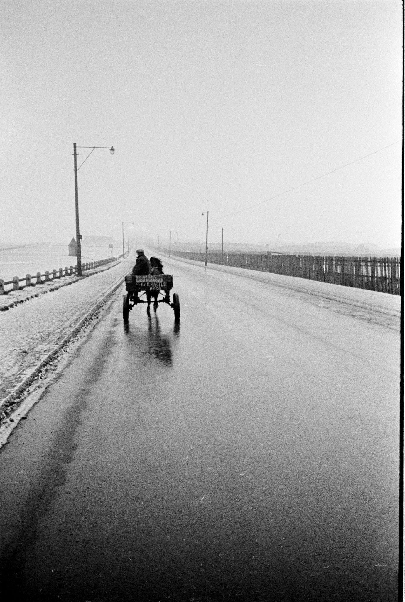 #39 A man rides on a horse drawn cart along the coast road between Seaton Carew beach and Hartlepool in County Durham, northeast England during winter 1962.