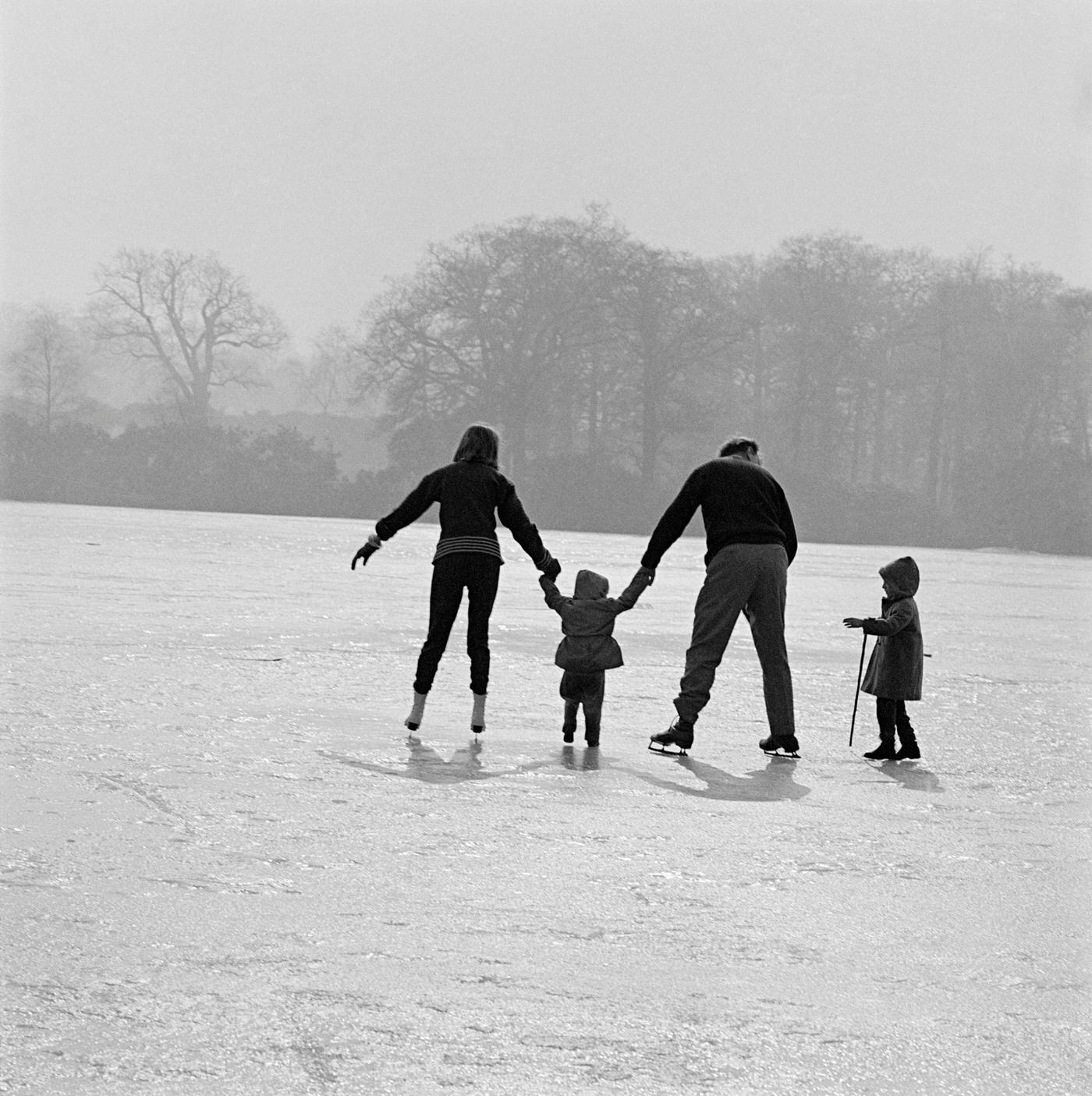 #2 Skating in Richmond Park, London, 1962. A man and woman on skates helping two small children to walk on the ice on a pond or lake in Richmond Park in winter.