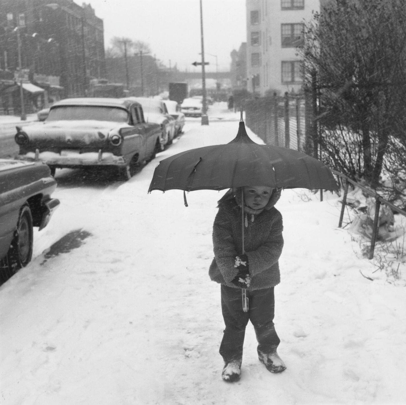 #8 Two-year-old Mary Olskey carries an umbrella as she takes tentative steps on the snow in the Astoria neighbourhood of the Queens borough of New York City, New York, 11th February 1964