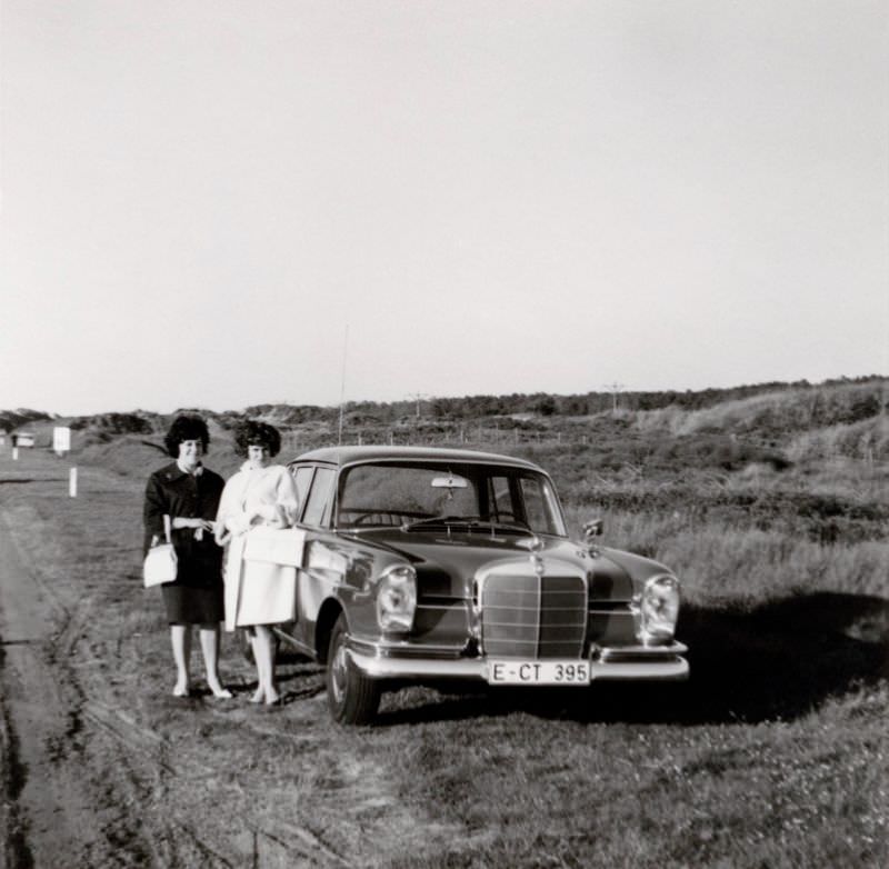 #26 Two stylish ladies, possibly sisters, posing with a Mercedes-Benz 220 S in the countryside. The car is registered in the West German city of Essen, 1965