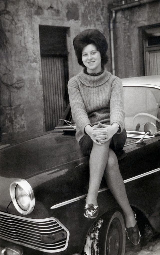A cheerful young lady posing on the fender of an Opel Rekord P2 on a snowy winter’s day, circa 1962