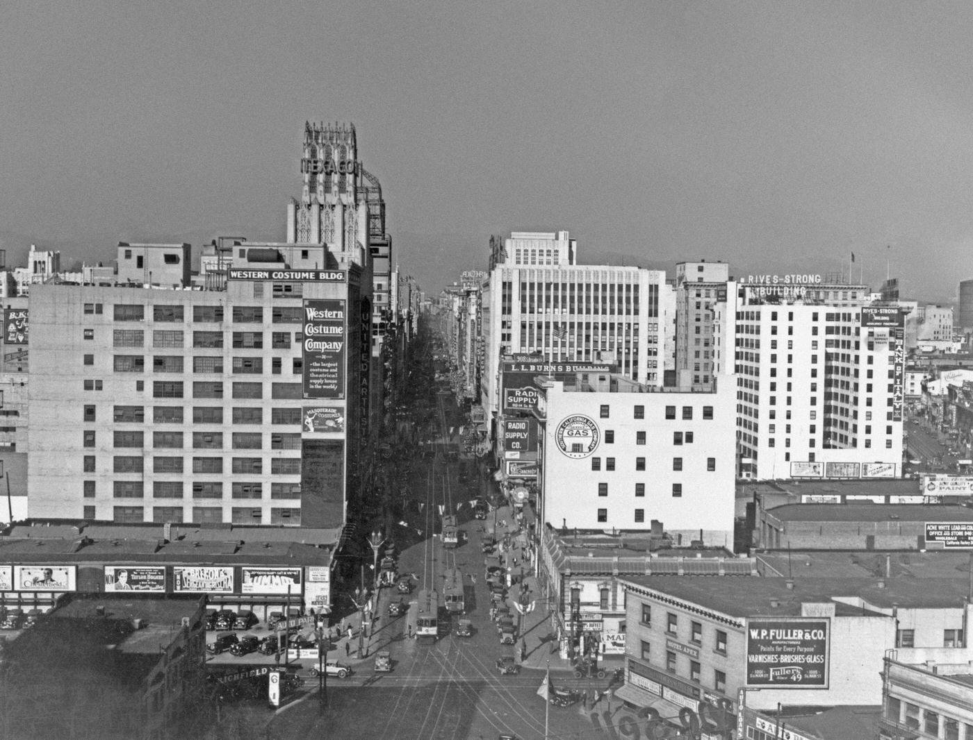 #134 High angle view looking north on Broadway from 11th Street, with the Western Costume Building on the left, with a Texaco sign beyond that, 1930