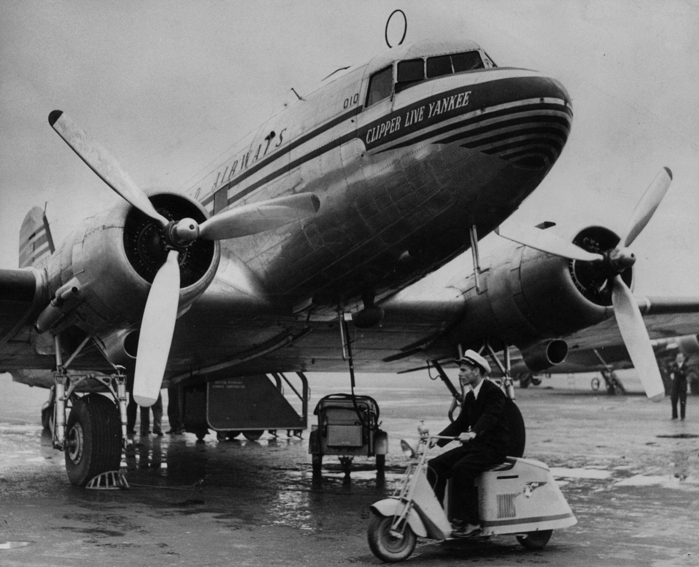 A motor-tricycle ‘scooter’ is being used for quick communication between airport buildings and planes at London Airport (Heathrow). One of the planes on the tarmac is a Pan-Am Clipper Line Yankee.