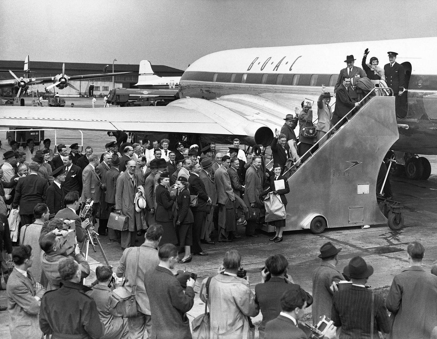 The first passengers of the world’s inaugural jet service board their plane bound for Johannesburg, while nearby reporters capture the event.