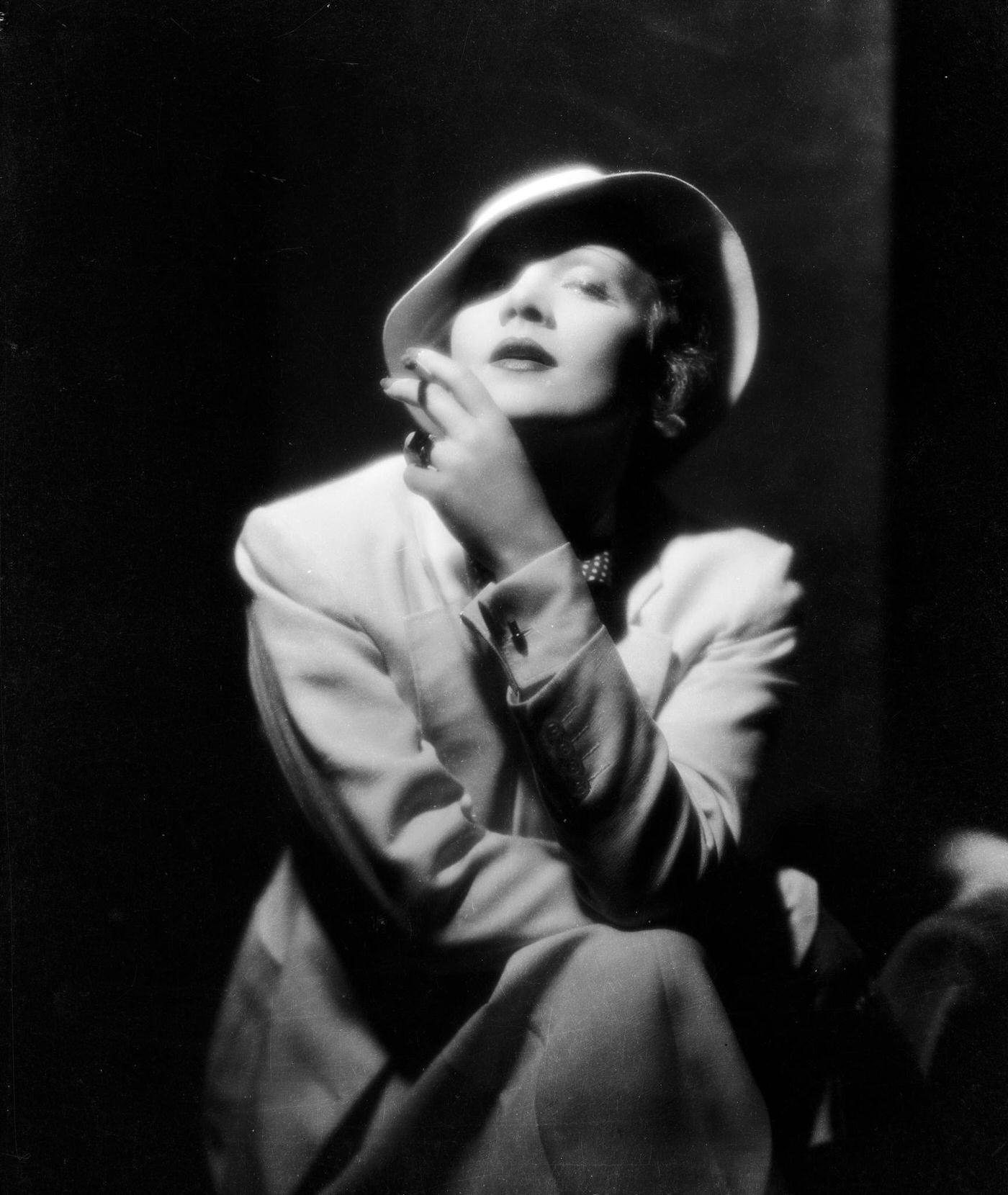 #57 Marlene Dietrich wears a soft pull-on hat while smoking a cigarette.