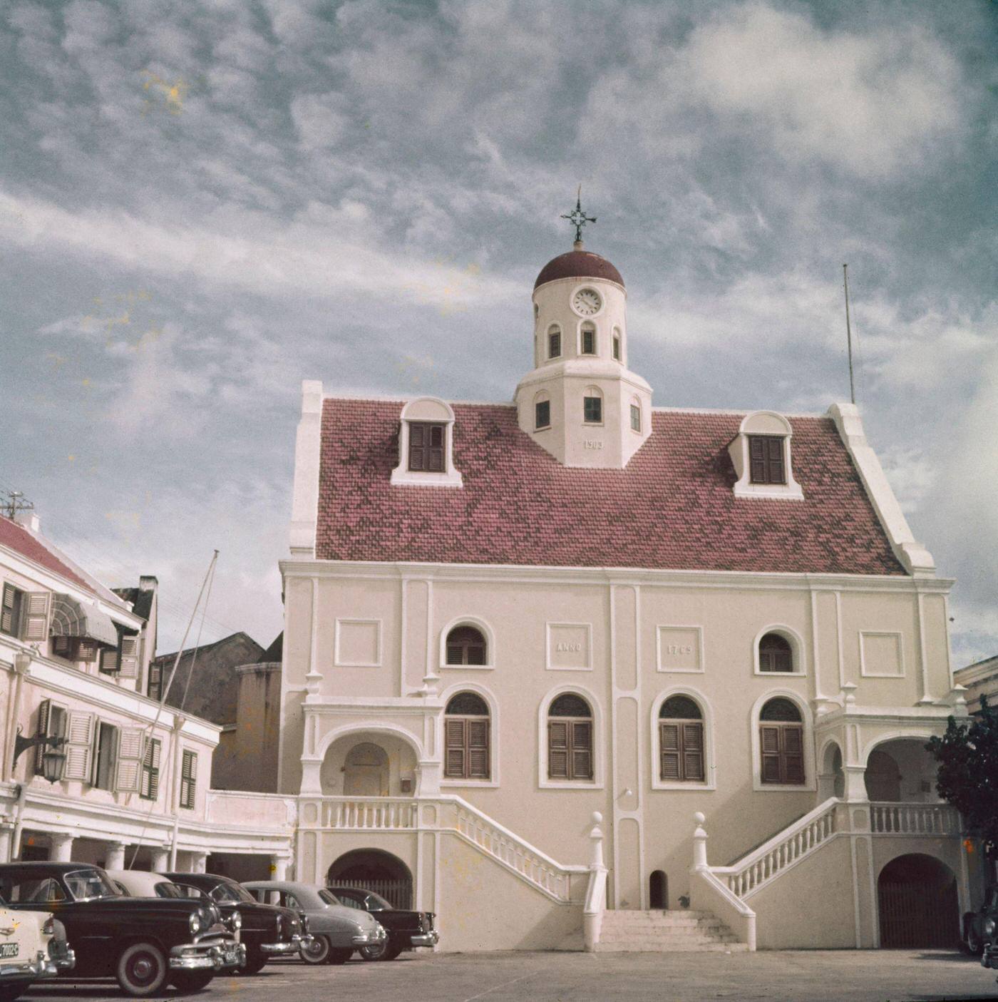 #12 Cars parked outside a Dutch colonial building in Willemstad, capital city of the island of Curaçao, part of the Kingdom of the Netherlands in the southern Caribbean Sea, 1955.