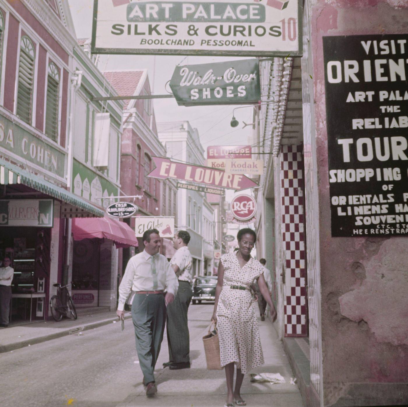 #13 Pedestrians and residents walking along a shopping street in Willemstad, capital city of the island of Curaçao, part of the Kingdom of the Netherlands in the southern Caribbean Sea, 1955.