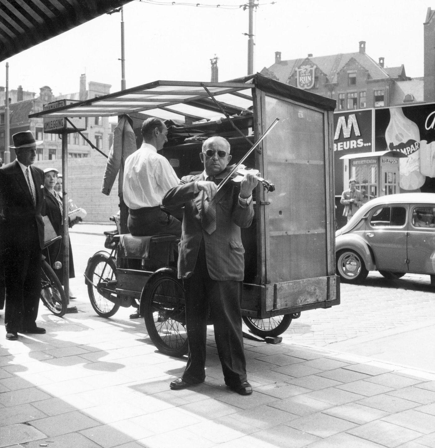 #21 Two musicians, one playing an organ and the other a violin, performing in a street in the Netherlands, 1955.