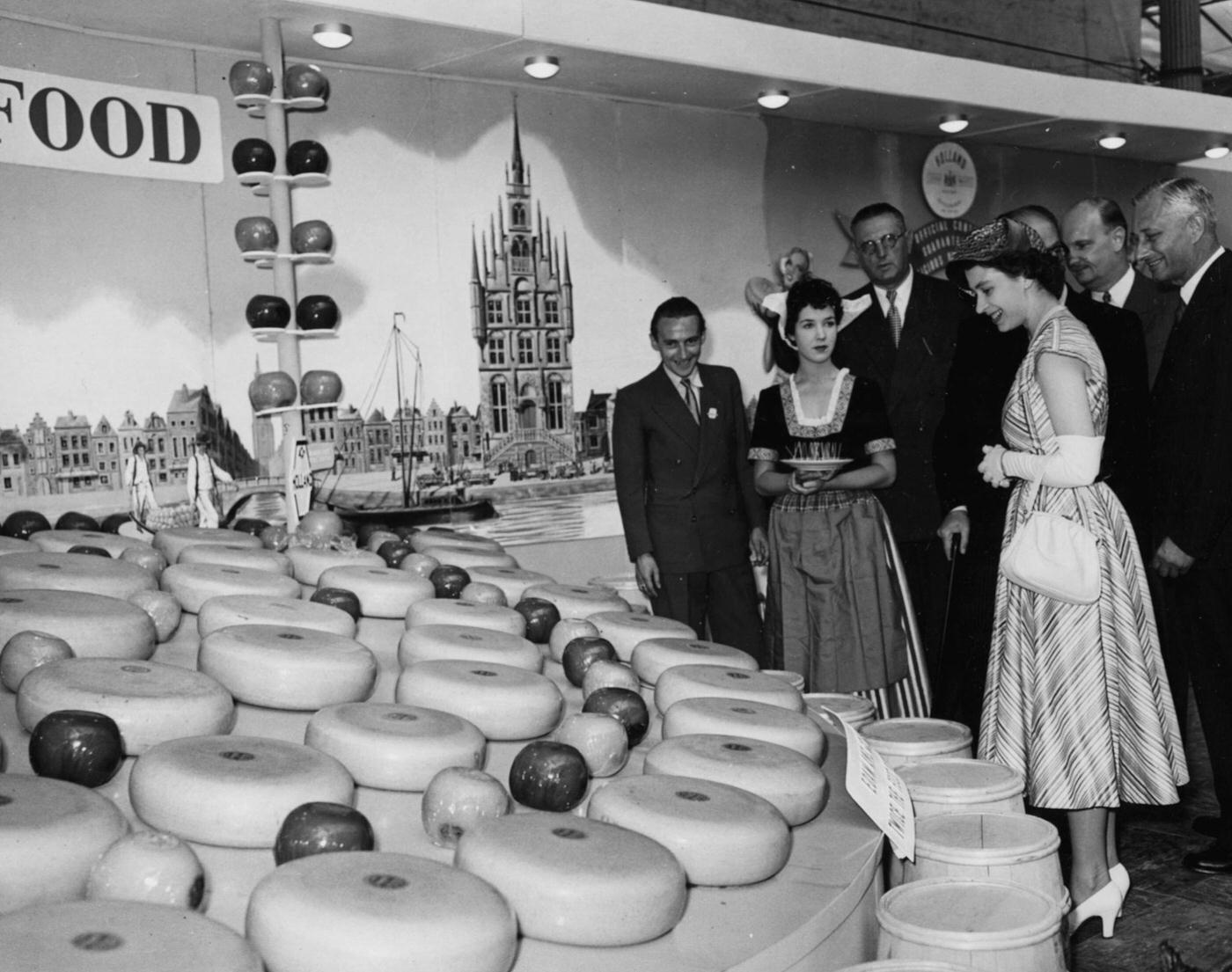 #35 Queen Elizabeth II admires a display of Dutch cheese wheels on the Netherlands exhibit at the British Food Fair at Olympia in London, 1952.