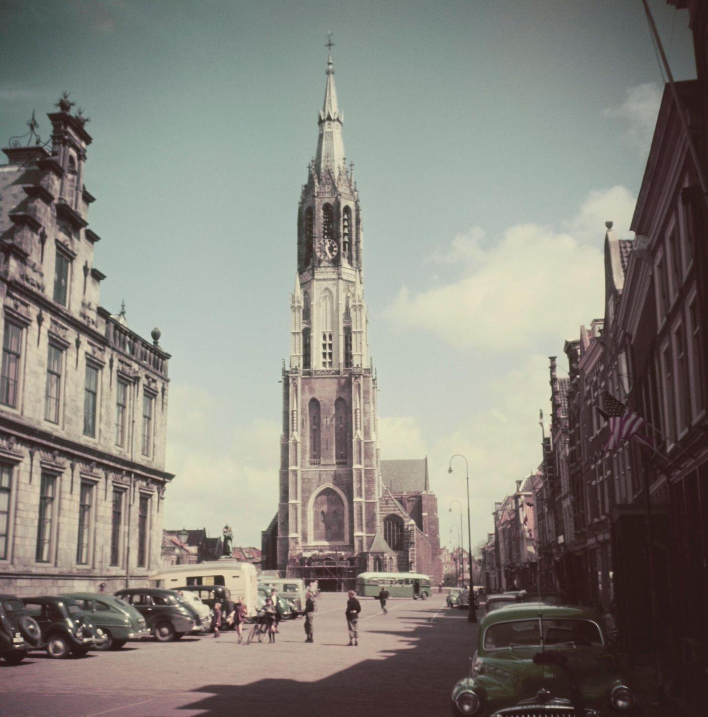 #44 Pedestrians pass cars parked beside City Hall on Markt Square in front of Nieuwe Kerk Protestant church in the center of the city of Delft in the province of South Holland in the Netherlands 1950.