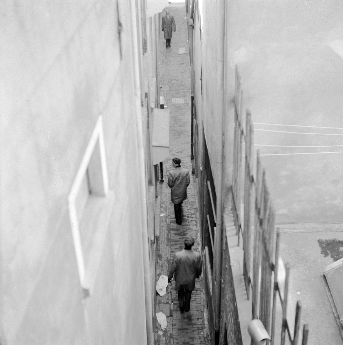 #9 Men walking down a narrow alley in the Netherlands, circa 1956.