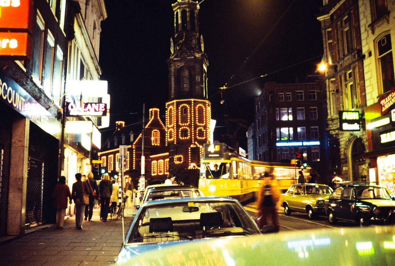 #19 Neon lights at night in the city center of Amsterdam, The Netherlands, during the 1970s-1980s. A yellow tramcar and Munttoren tower are visible.