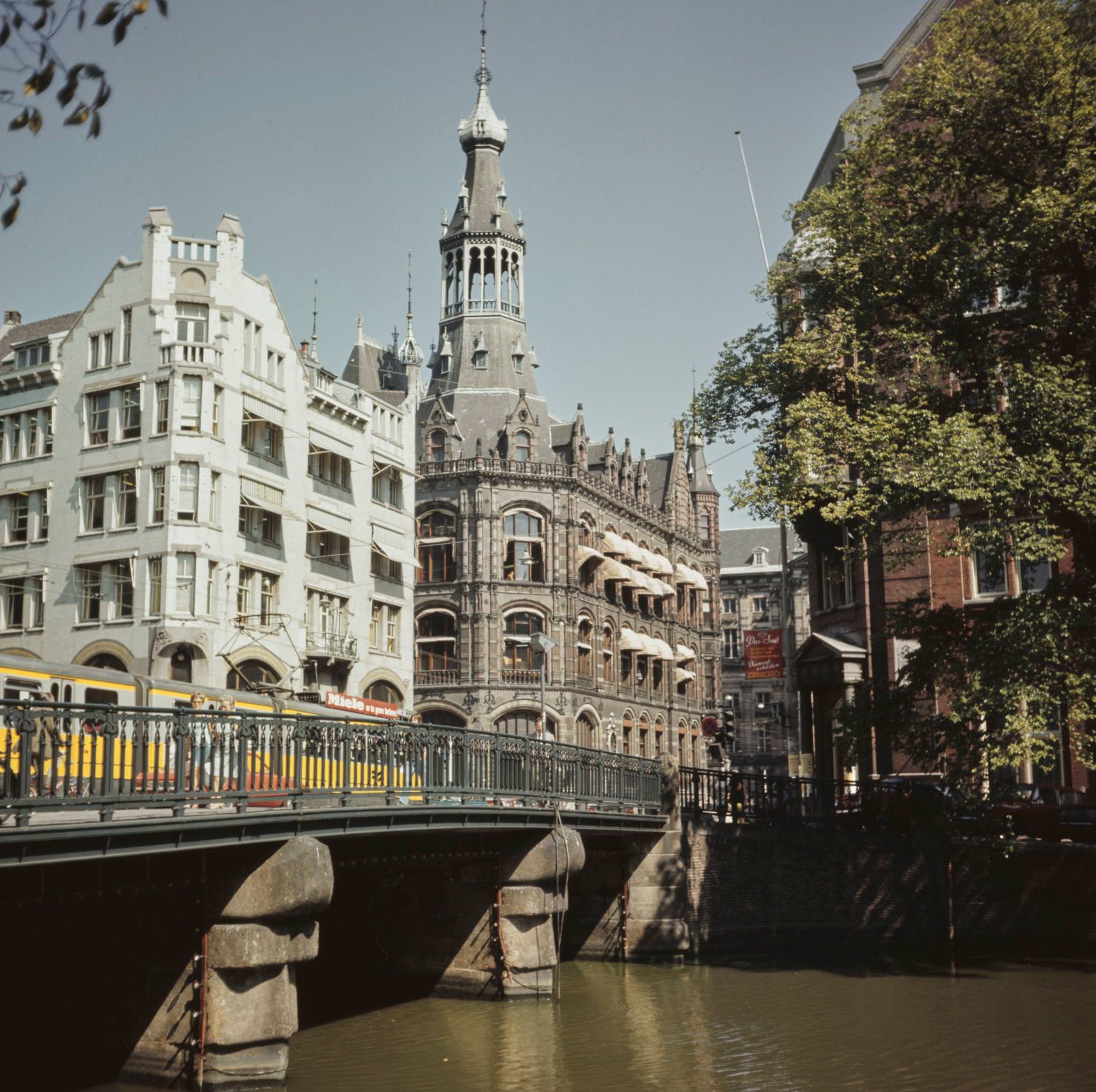 #73 A tram runs along Raadhuisstraat on a bridge over Singel Canal in front of the Central Bank and Old General Post Office in the center of Amsterdam, capital city of the Netherlands, 1970
