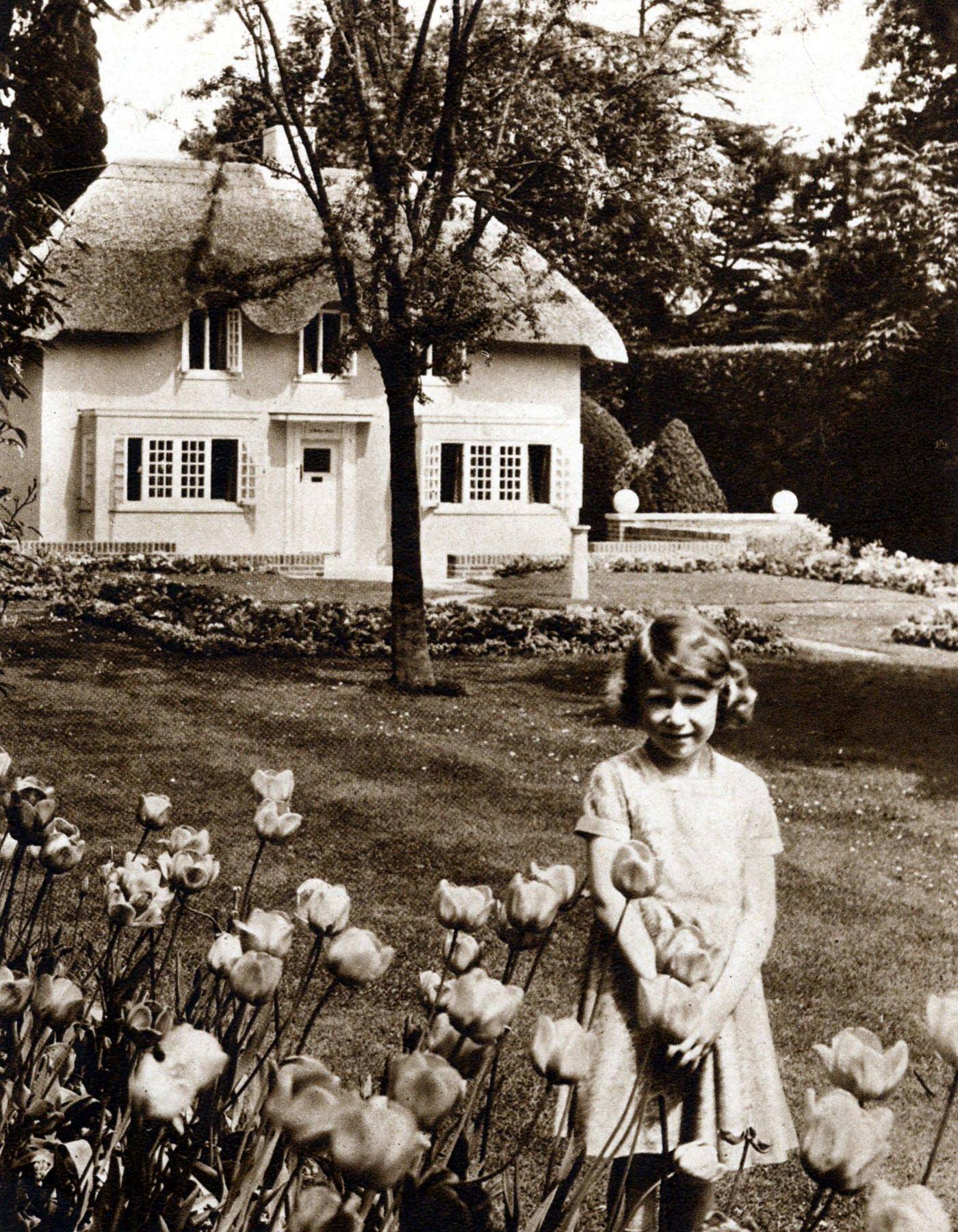 #20 Princess Elizabeth as a child in the garden of the Royal Lodge, Windsor with Y Bwthyn Bach (The Little House), the playhouse given to her by the people of Wales.