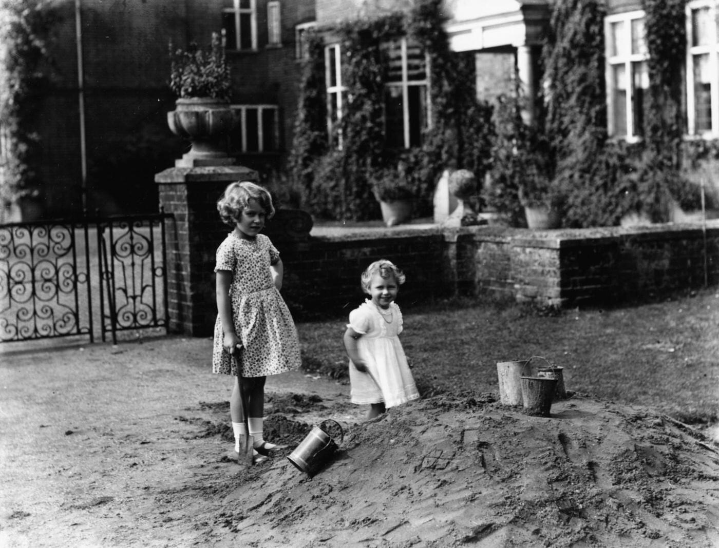 #40 Princess Elizabeth (left) and Princess Margaret playing together outdoors beside a pile of sand, August 12th 1932.