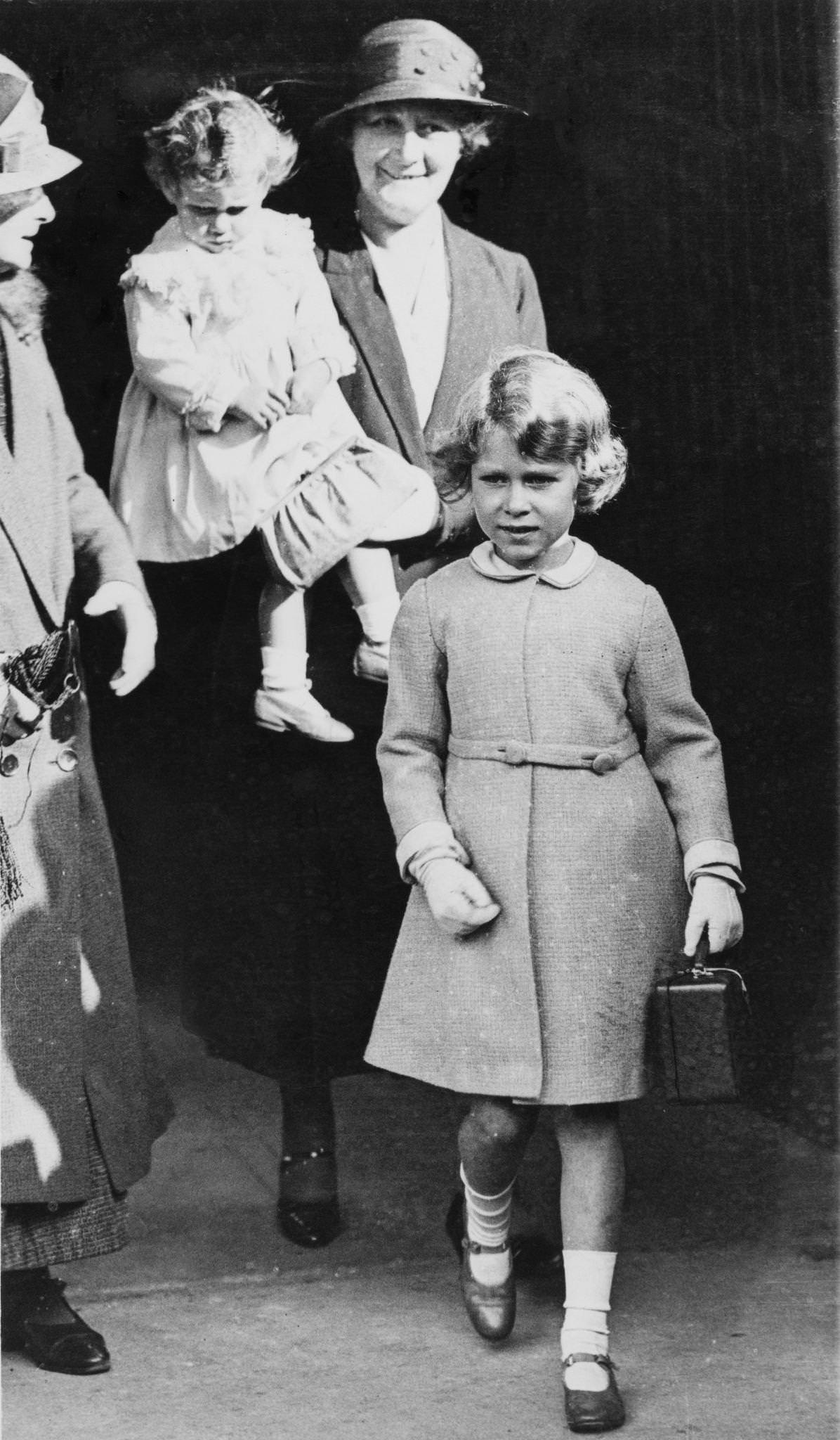 #41 Princess Elizabeth and Princess Margaret arrive at Ballater railway station in Aberdeenshire, Scotland on August 21, 1932. Princess Elizabeth carries her own little attache case while Princess Margaret is in the arms of royal nanny Clara Knight.