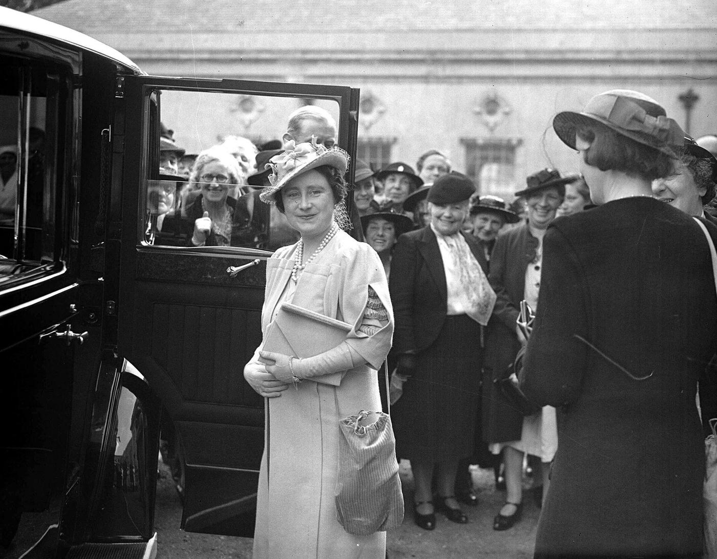 #97 Queen Elizabeth carrying both her handbag and gas mask after visiting the Woodford, Essex Clearing House of the central hospital supply service during WWII, May 24, 1940.