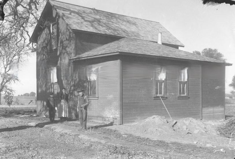 #86 View of three people standing in front of a house, 1890