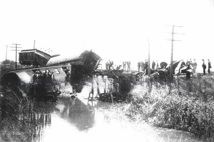 #62 Train wreck over a slough in Sacramento. Groups of men standing on the bank of the slough, bridge and on the wrecked cars and locomotive, 1890