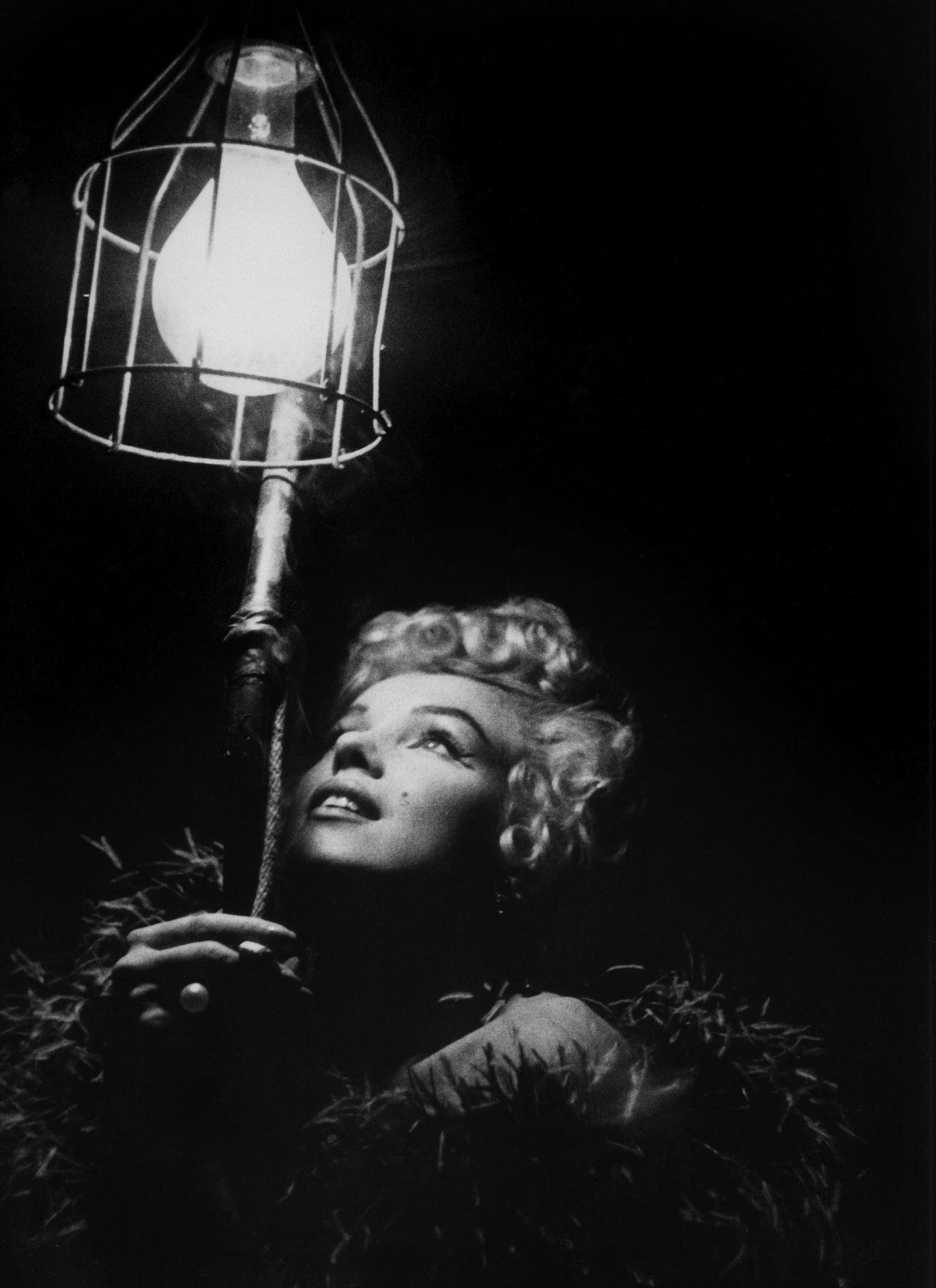 Marilyn Monroe wearing a feather boa looks up into a bright light in 1954 during the filming of “The Seven Year Itch”