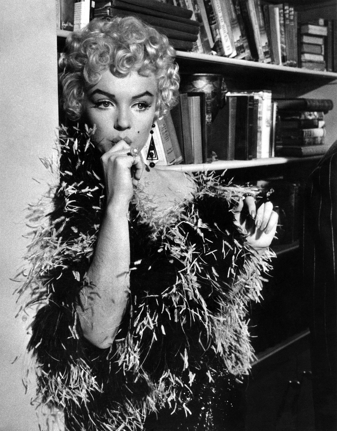 Marilyn Monroe stands in front of a bookcase wearing a feather boa in 1954 during the filming of “The Seven Year Itch”