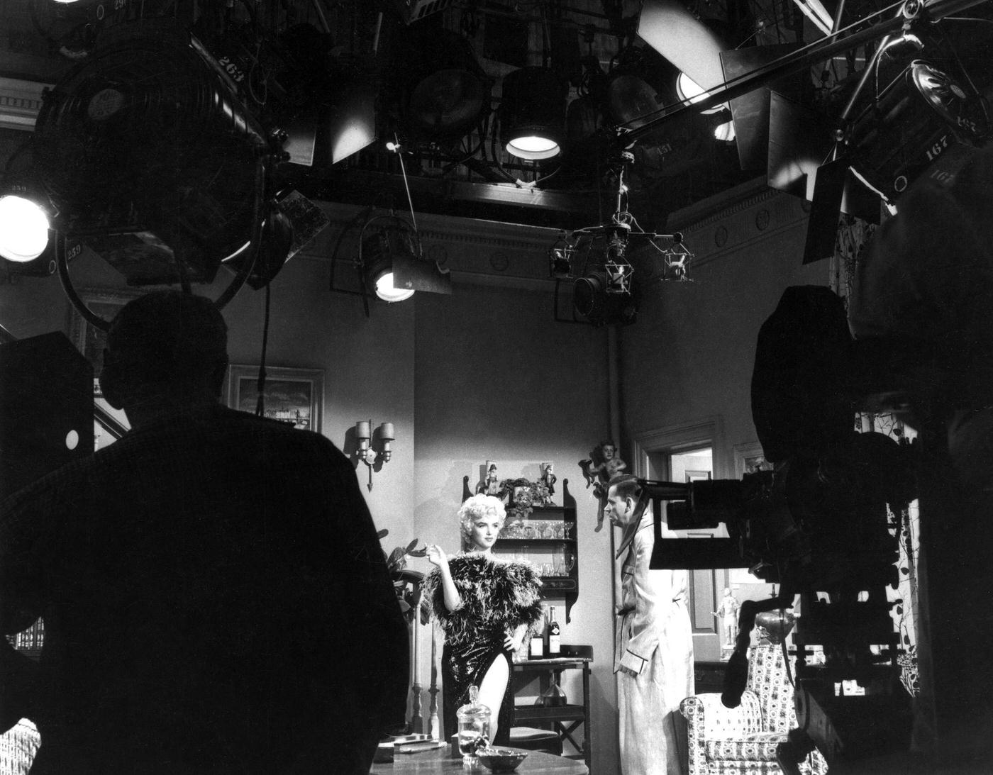 Marilyn Monroe wearing a feather boa with co-star Tom Ewell with cameras and equipment in the foreground during the filming of “The Seven Year Itch” in 1954