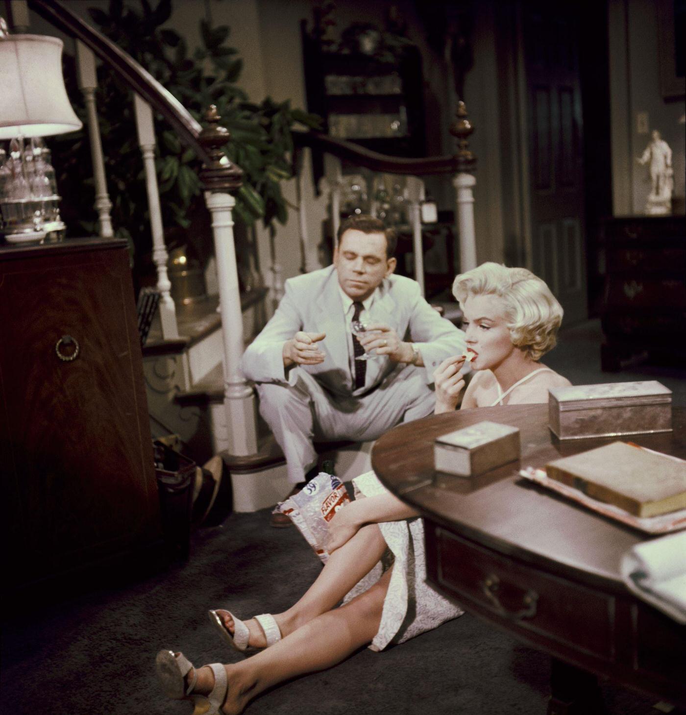 Marilyn Monroe stands in the entrance of an apartment set wearing a polka-dot dress and holding groceries and a desk fan in 1954 during the filming of “The Seven Year Itch”