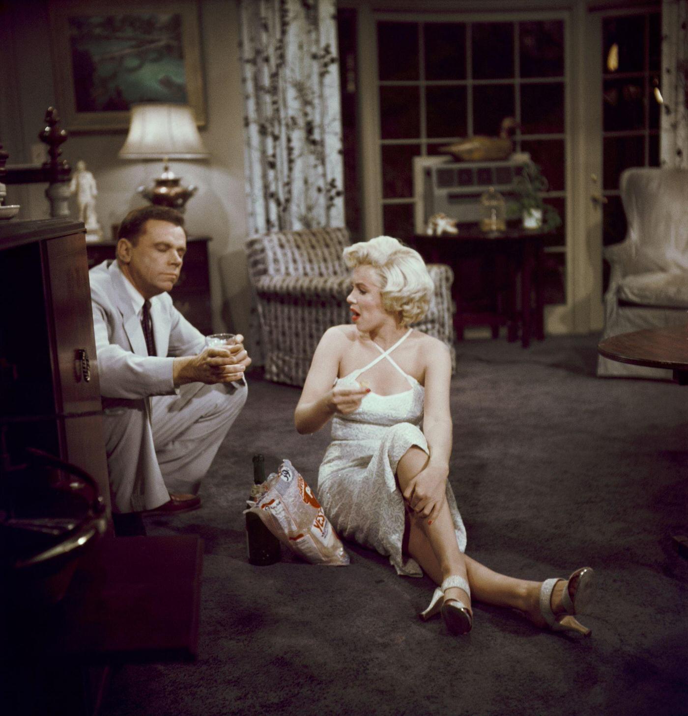 Marilyn Monroe eats potato chips and drinks champagne sitting on the floor with co-star Tom Ewell in 1954 during the filming of “The Seven Year Itch”