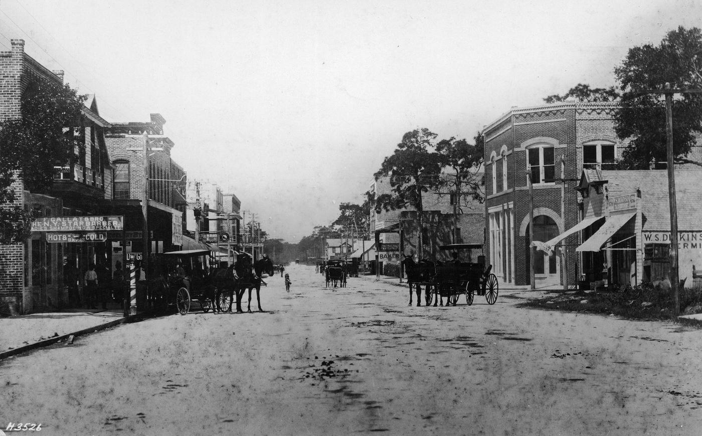 #28 Horses, carriages, and pedestrians are seen as one looks West along the shops which line unpaved Flagler Street, Miami, Florida, circa 1900.