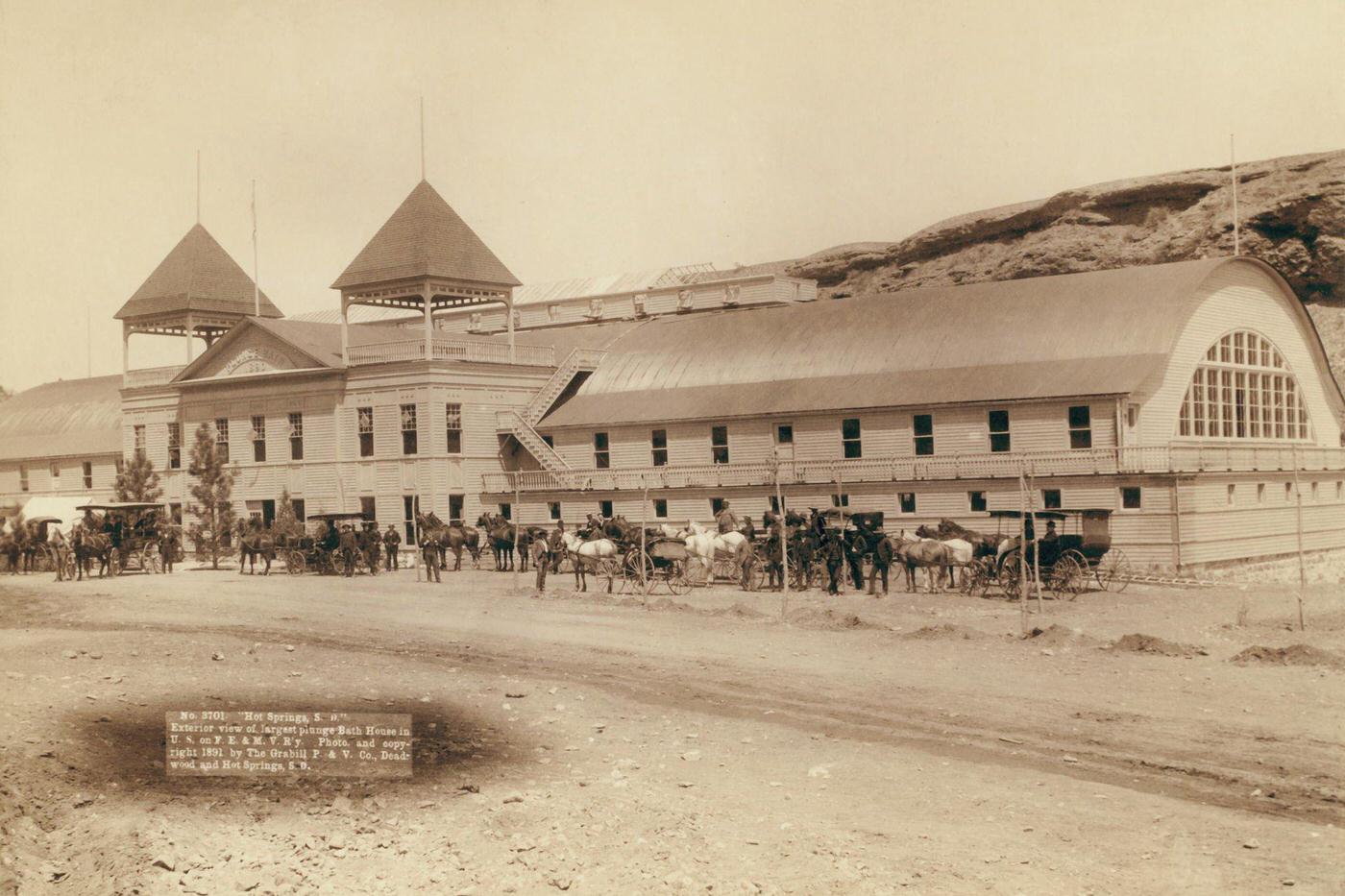 #48 Hot Springs Bath House, United States, circa 1890: Exterior view of largest plunge bath house in U.S. on F.E. and M.V. Railway; Large building with several horses and carriages in front.
