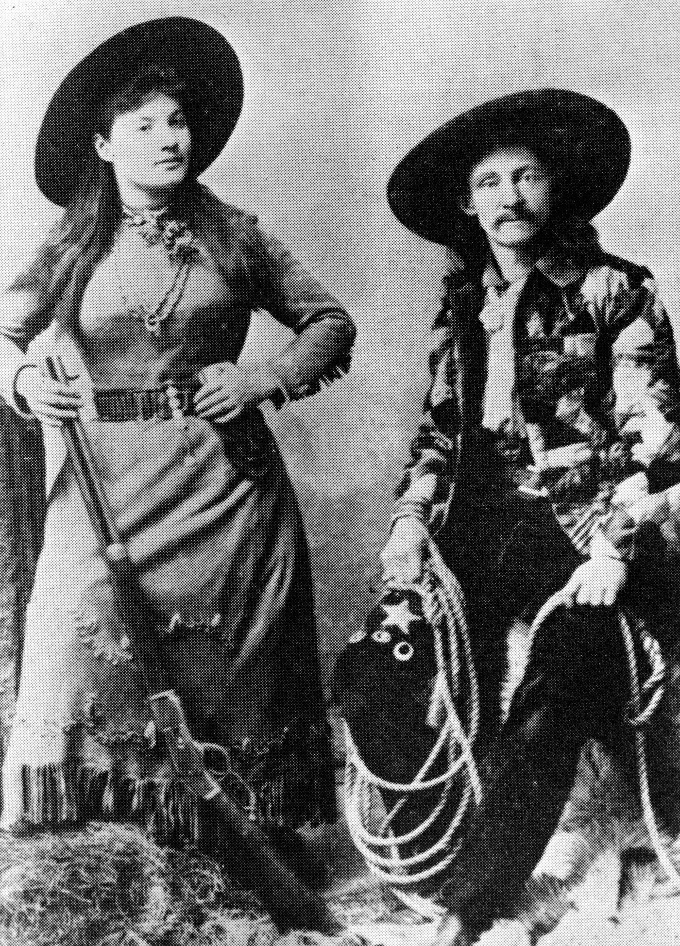 #50 Publicity portrait of Annie Oakley & Texas Bill, late 1800s: American sharpshooter Annie Oakley (1860 – 1926) poses with one knee on a haybale and a shotgun on her hand, while Texas Bill Shufflebottom sits on a haybale with a lasso over his knee. The photograph was used to advertise her performances with Buffalo Bill’s Wild West Show.