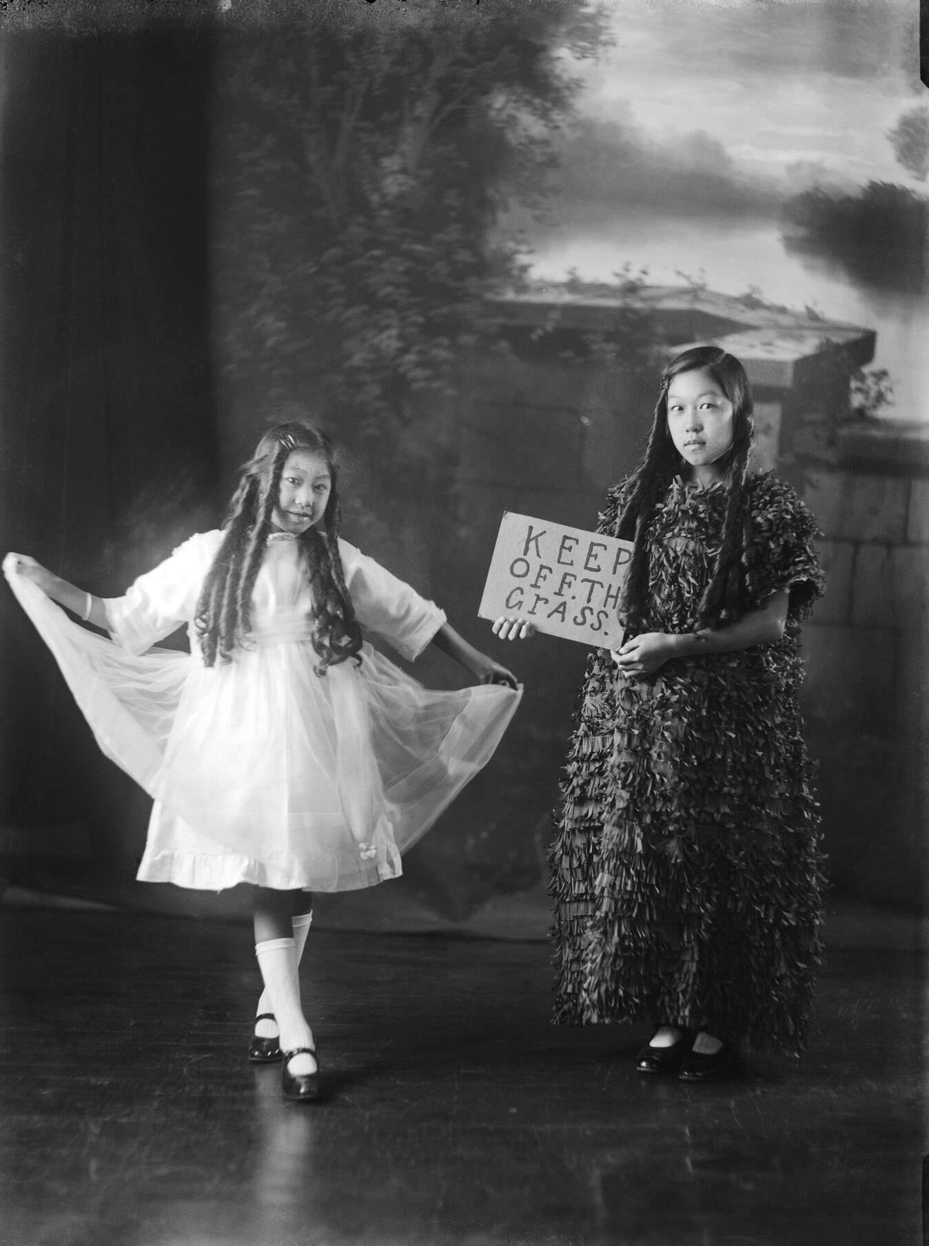 #35 Two girls in fancy dress, one holding a sign saying ‘Keep off the grass’
