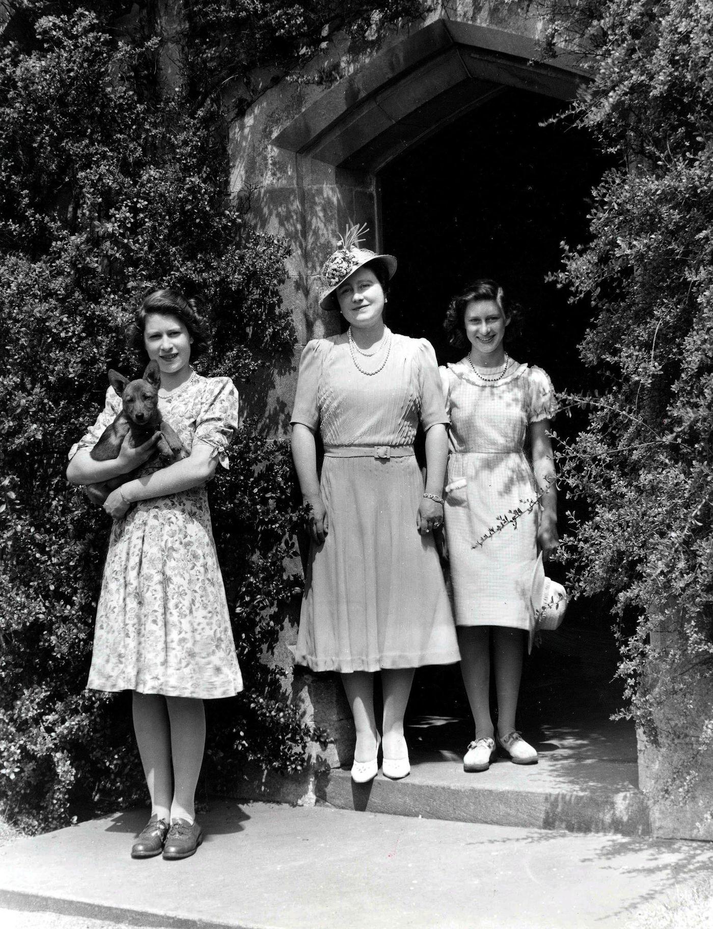 #22 Queen Elizabeth The Queen Mother with her two daughters, Princess Margaret (right) and Princess Elizabeth (later Queen Elizabeth II), holding a dog, during World War Two, 1940.