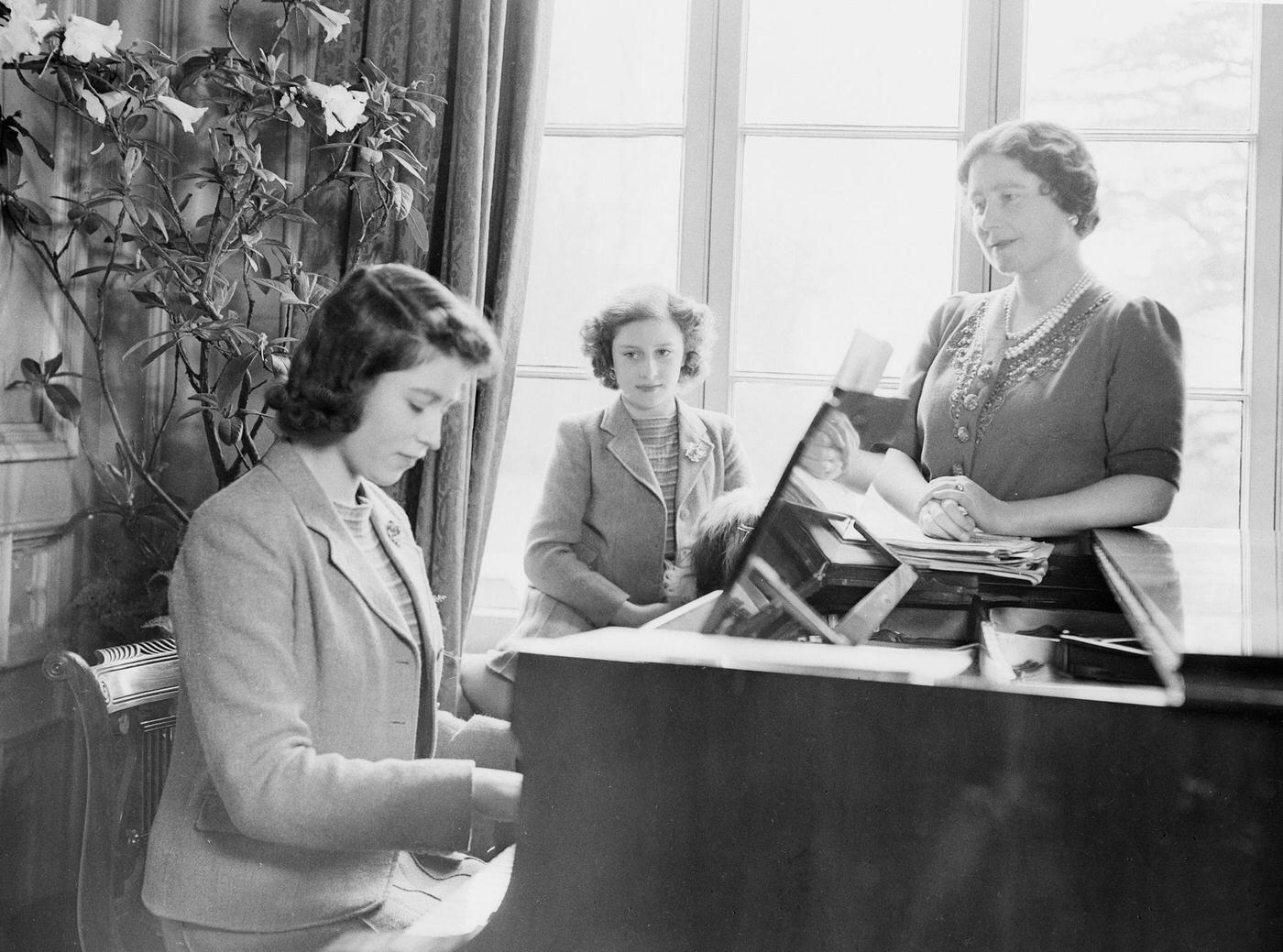 #59 Princess Elizabeth plays the piano as Queen Elizabeth and Princess Margaret look on at the Royal Lodge in Windsor Castle, England on April 11, 1942.