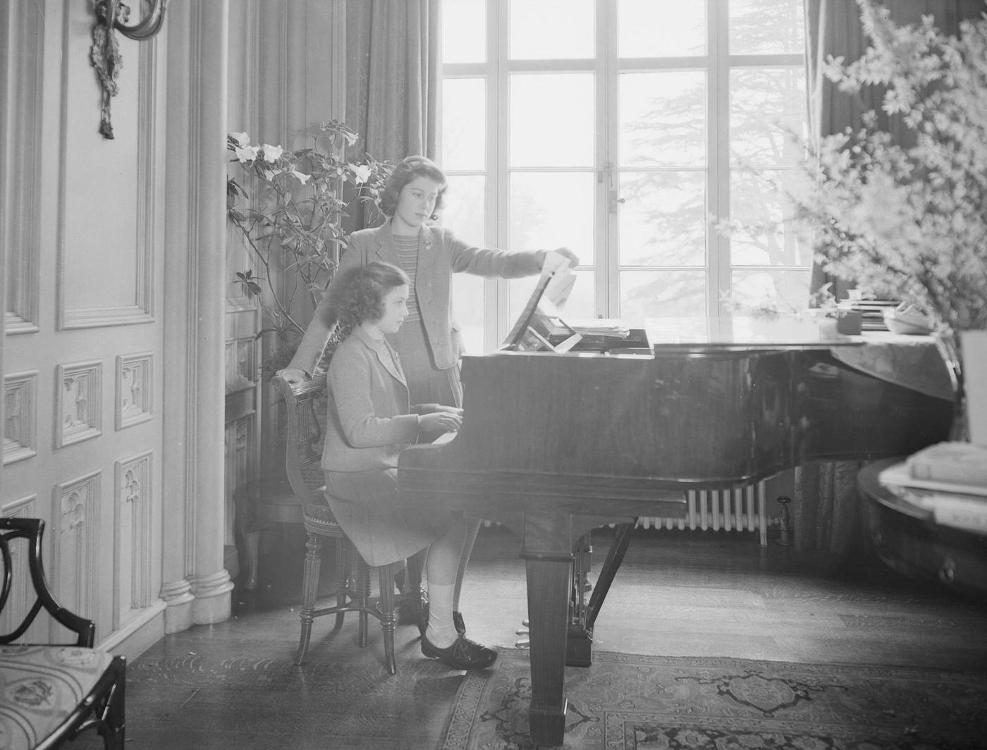 #60 Princess Elizabeth looks on as Princess Margaret plays the piano at the Royal Lodge in Windsor Castle, England on April 11, 1942.