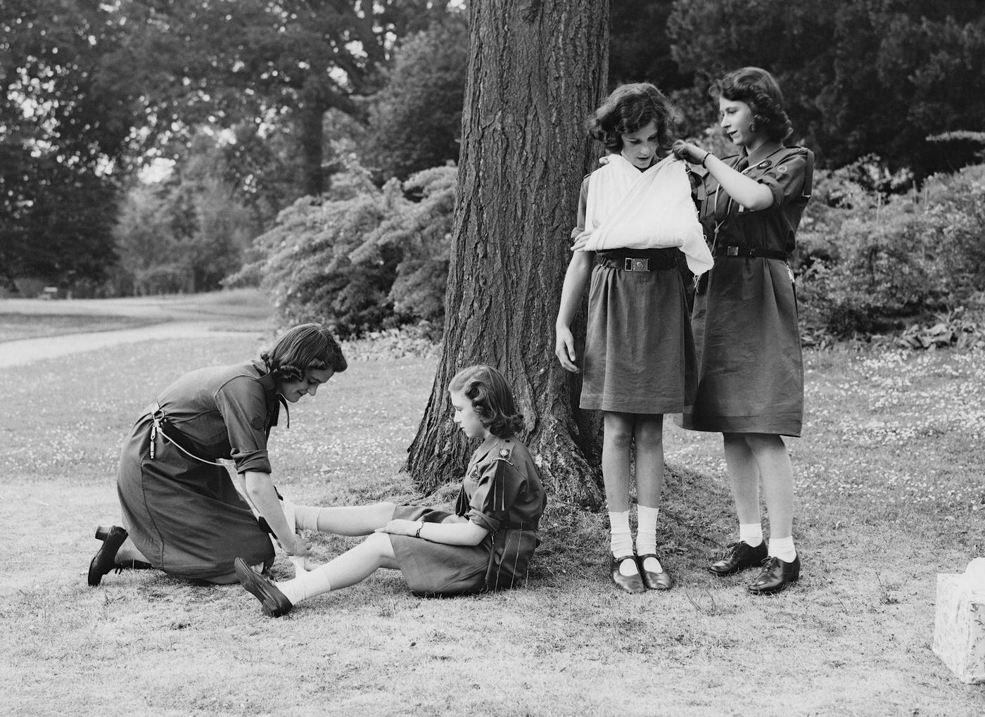 #64 Princess Elizabeth places a young girl’s arm in a sling as part of the girl guides in Frogmore, Windsor, England on April 11, 1942.