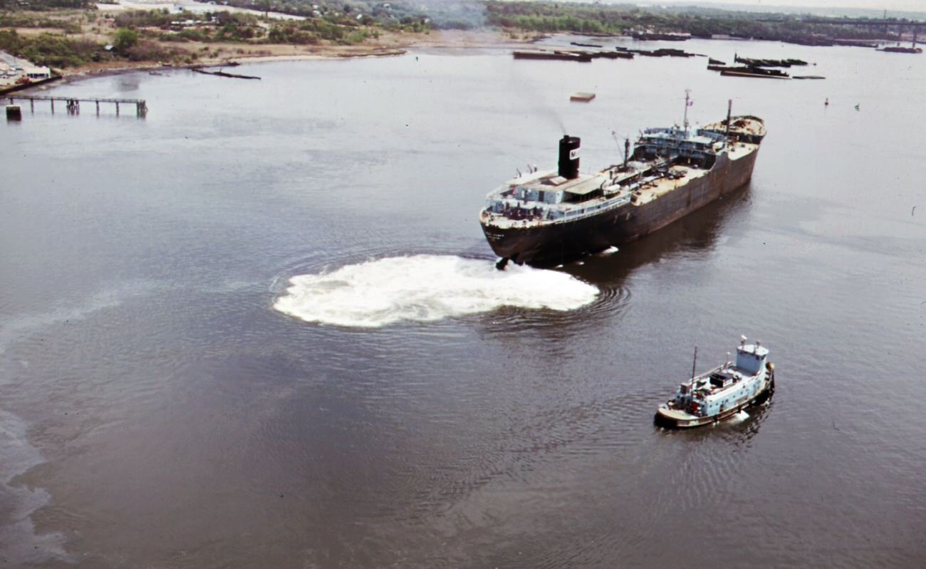 #104 Mobile oil tanker and tug boat on arthur kill–the waterway between new jersey and staten island which is the site of a huge petrochemical manufacturing complex, 1970s