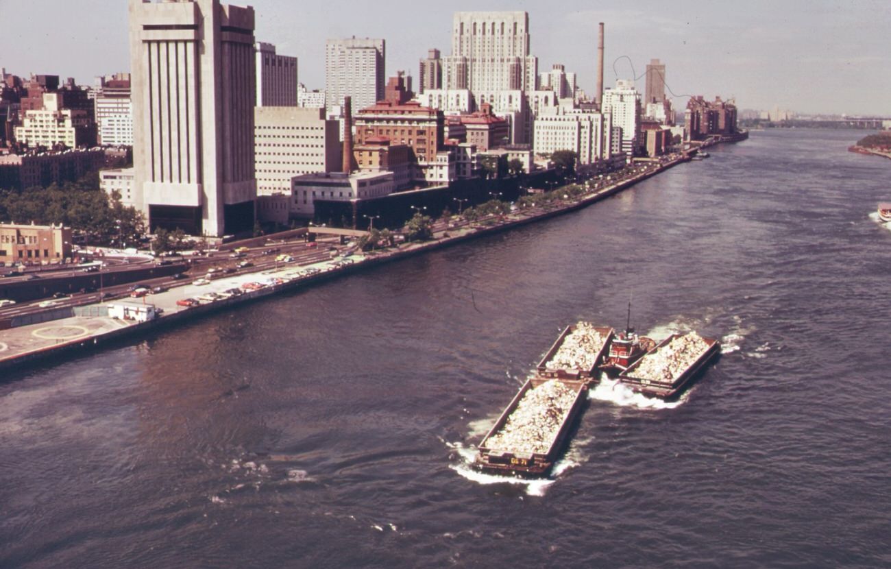 #112 Part of the 26,000 tons of solid waste that new york city produces each day. Tugs tow heavily-laden barges down the east river to the overflowing staten island landfill, 1970s