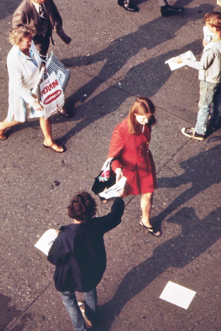 #68 Without breaking stride, homeward bound commuter at the staten island ferry terminal reaches for leaflet from street distributor, 1970s