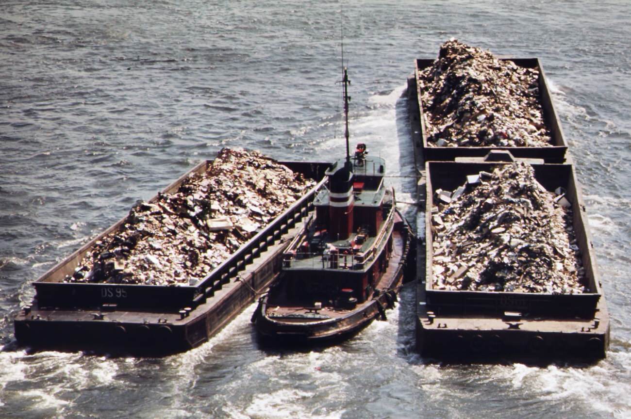 #77 Tugboat herds garbage scows down the east river from a transfer point in manhattan. Destination is the staten island landfill, 1970s