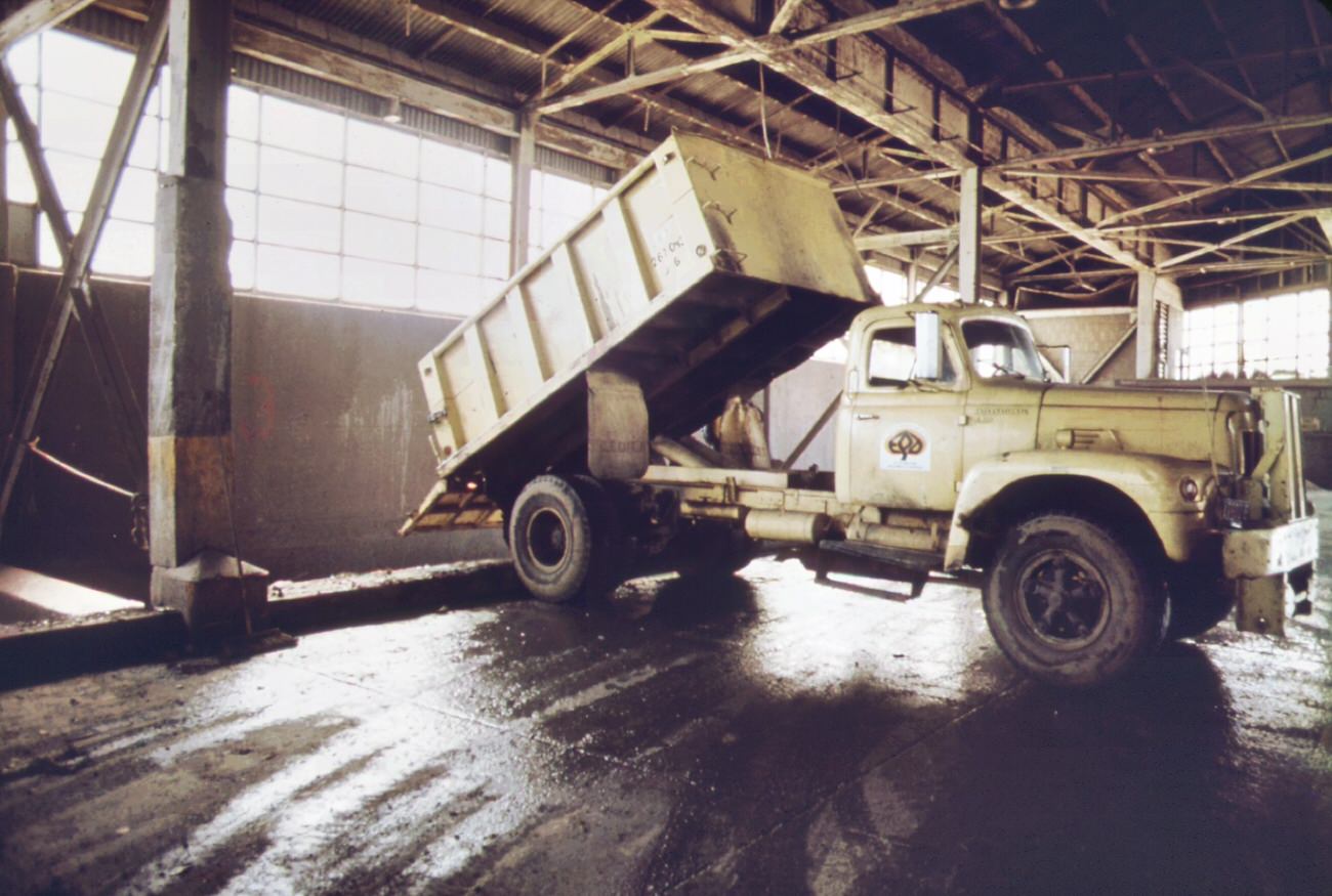 #92 Truck at the 91st street marine transfer station empties garbage into barge for trip down the east river to the staten island landfill dumping site, 1970s