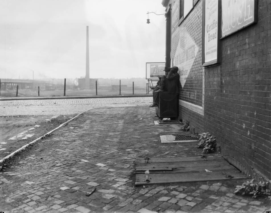 #160 View of two men sitting on a cupboard beside a building at Leonard Street and Market Street. Blue Valley Butter sign is visible, 1930