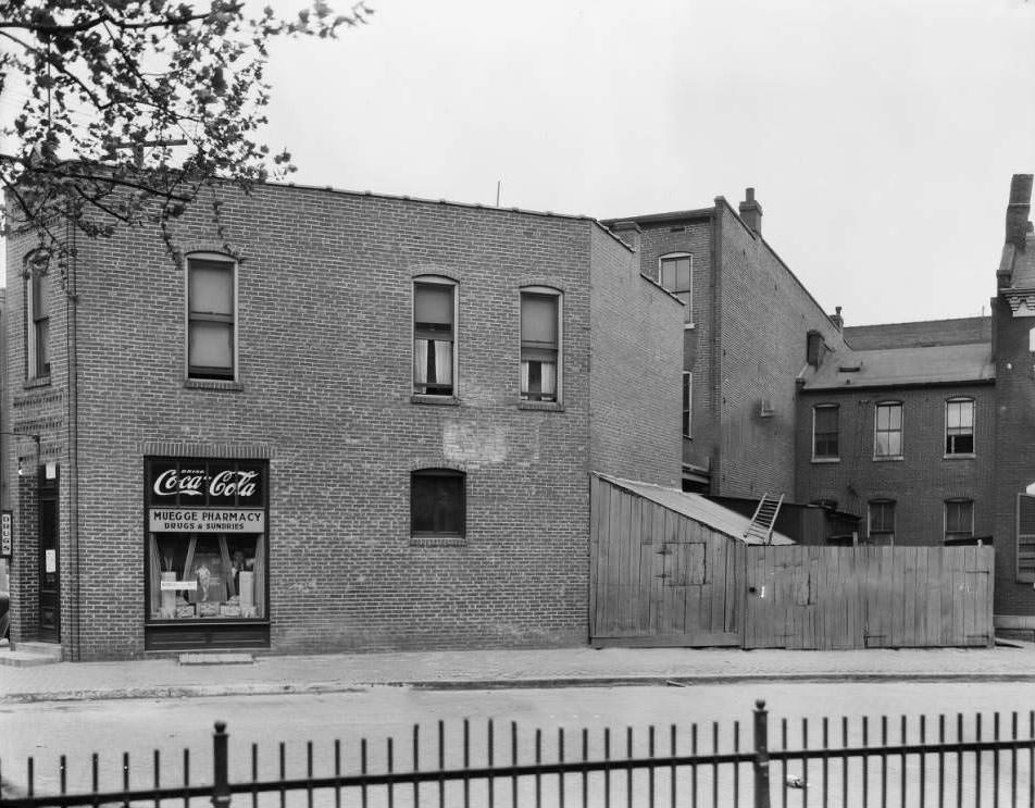 #12 View of the building that housed Muegge Pharmacy in Old North St. Louis, with two men looking out the window, 1930
