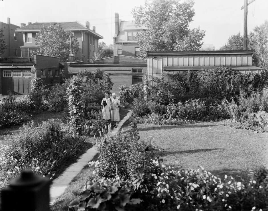 #18 View of backyard garden at 5228 Westminster Place in Central West End, with two women and a small black dog visible, 1931