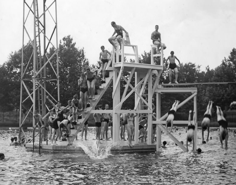 #197 Boys and girls of all ages swarm over the diving tower at the Marquette Pool as it opens for the season, 1930