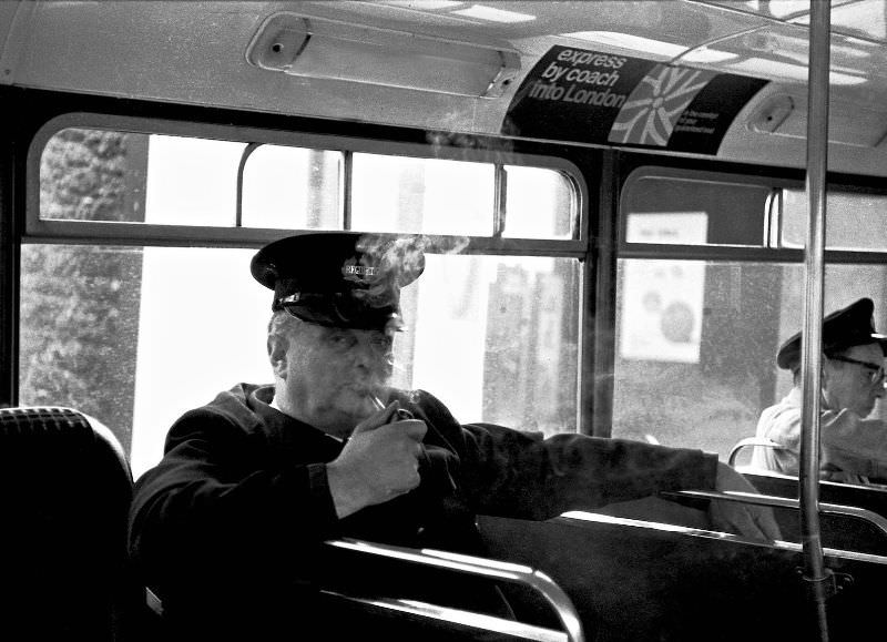 #40 Weary regulator enjoys a well-deserved pipe in a waiting bus, Paignton bus station, 1970