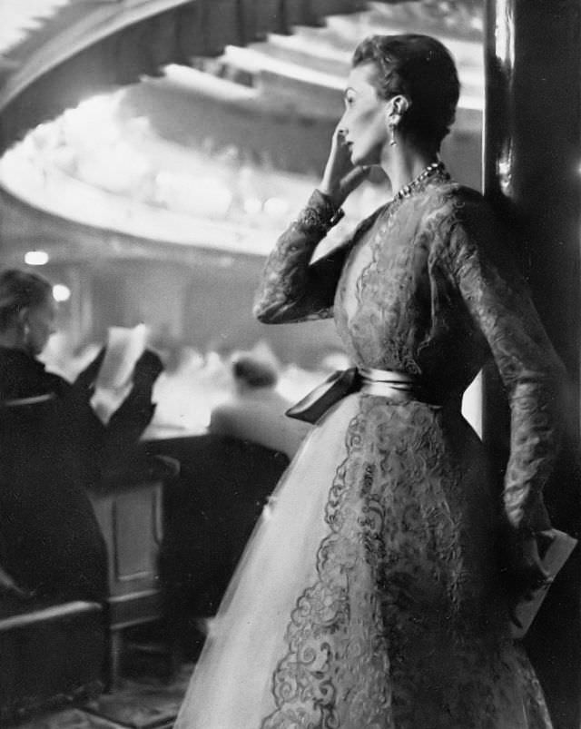 #17 Barbara Goalen in ballerina-length dress in pale caramel tulle, over it a coat of deep coffee lace fastened with a turquoise satin sash by Harald after Dior, 1951.